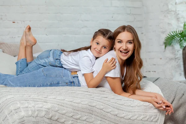Innenporträt einer schönen Mutter mit ihrer charmanten kleinen Tochter, die vor dem Schlafzimmer posiert. — Stockfoto