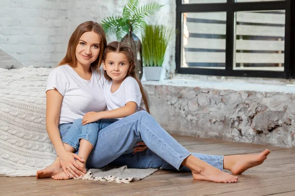 Indoor portrait of a beautiful mother with her charming little daughter posing against bedroom interior.