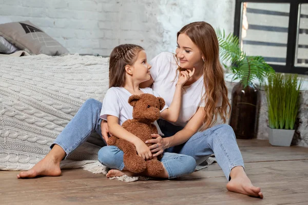 Innenporträt einer schönen Mutter mit ihrer charmanten kleinen Tochter, die vor dem Schlafzimmer posiert. — Stockfoto