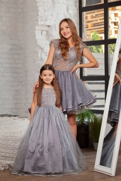 Indoor portrait of a beautiful mother with her charming little daughter posing against bedroom interior.