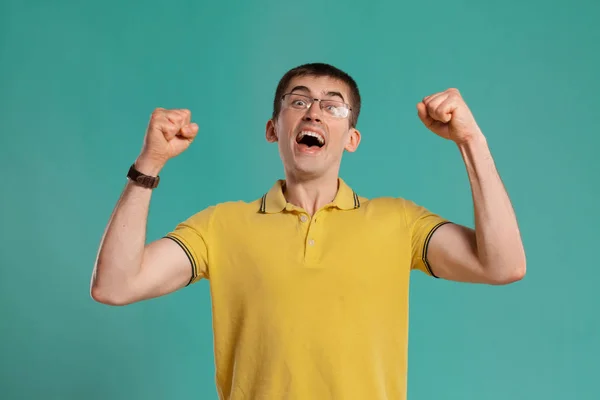 Chico guapo con una camiseta casual amarilla posando sobre un fondo azul . — Foto de Stock