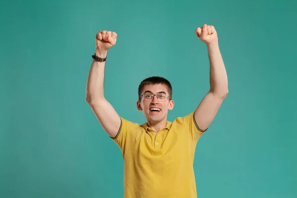 Chico guapo con una camiseta casual amarilla posando sobre un fondo azul . — Foto de Stock