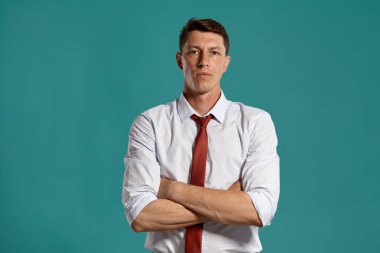 Klasik beyaz gömlekli ve kırmızı kravatlı genç adam mavi arka planda poz veriyor..