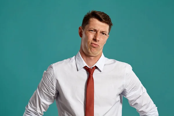 Jongeman in een klassiek wit shirt en rode stropdas poserend over een blauwe achtergrond. — Stockfoto