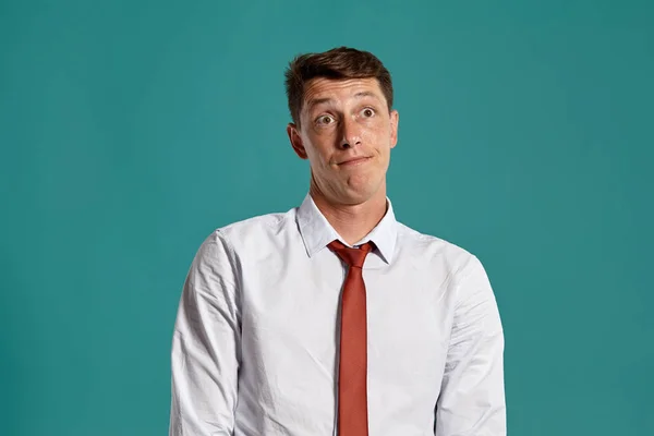 Hombre joven con una camisa blanca clásica y corbata roja posando sobre un fondo azul . — Foto de Stock