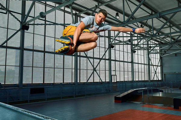 Rollerblader saltar alto desde la gran rampa de aire realizar truco. Equipo de parque de skate interior . — Foto de Stock