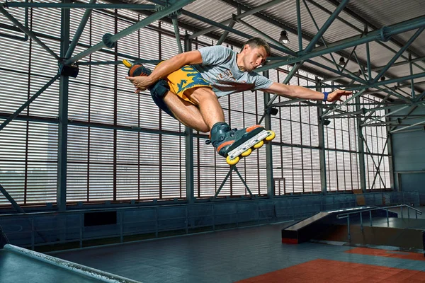 Rollerblader skáče vysoko od velkého triku na vzduchové rampě. Interiérech zařízení na bruslit. — Stock fotografie