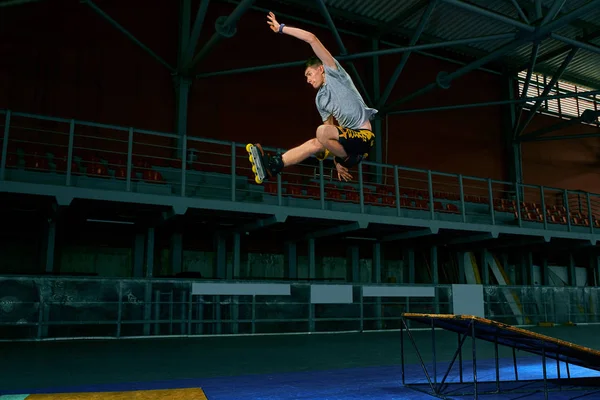 Rollerblader skáče vysoko od velkého triku na vzduchové rampě. Interiérech zařízení na bruslit. — Stock fotografie