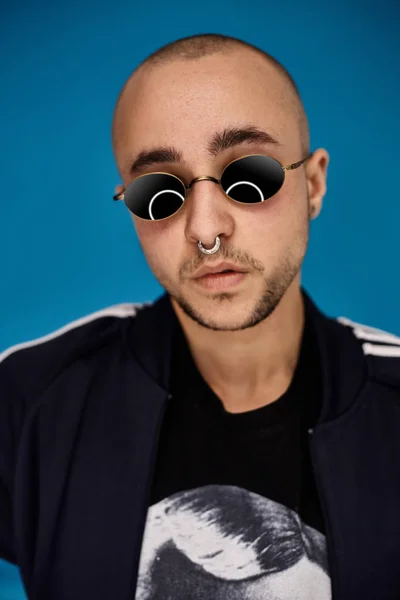 Estúdio de um jovem careca tatuado posando contra um fundo azul. Estilo dos anos 90 . — Fotografia de Stock