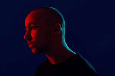 Mavi bir arka plan aleyhine poz veren genç, dövmeli kel bir adamın stüdyo fotoğrafı. 90'ların stili.