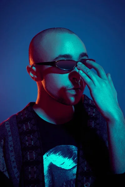 Fotografía de un joven calvo tatuado posando sobre un fondo azul. Estilo de los años 90 . — Foto de Stock