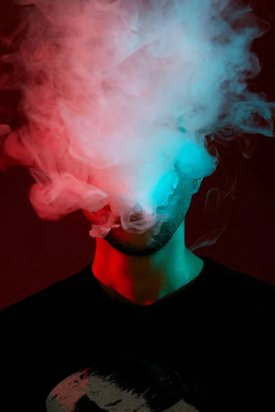 Primer plano del estudio de un joven calvo vapeando, soplando una nube de humo sobre el fondo rojo . — Foto de Stock