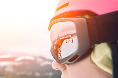 Kayak merkezinde kask ve dağların yansıması ile gözlük giyen snowboardcu kadının yakın portresi. Güneş parlaması