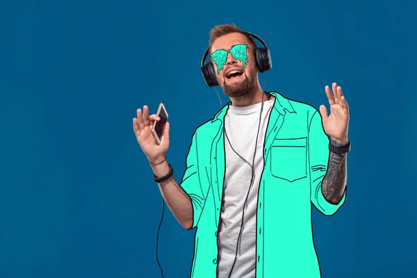Νέος άντρας με ένα απλό πουκάμισο κινουμένων σχεδίων και γυαλιά τήξης ακούει τη μουσική και τραγουδά σε ένα μπλε φόντο. — Φωτογραφία Αρχείου
