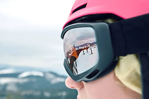 Közelről portré a snowboardos nő a sípálya visel sisakot és védőszemüveget tükörképe hegyek. — Stock Fotó