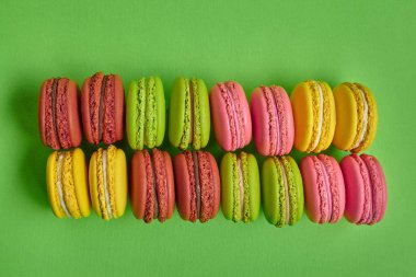 Renkli badem kurabiyesi ya da badem kurabiyesi, yeşil arka planda tatlı kremalı şekerleme. Yakın plan, kopyalama alanı.