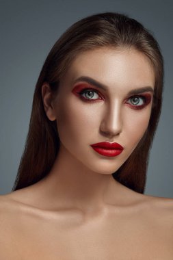 Gri bir arkaplan üzerinde parlak makyajlı, güzel, yarı çıplak bir mankenin göz kamaştırıcı portresi..