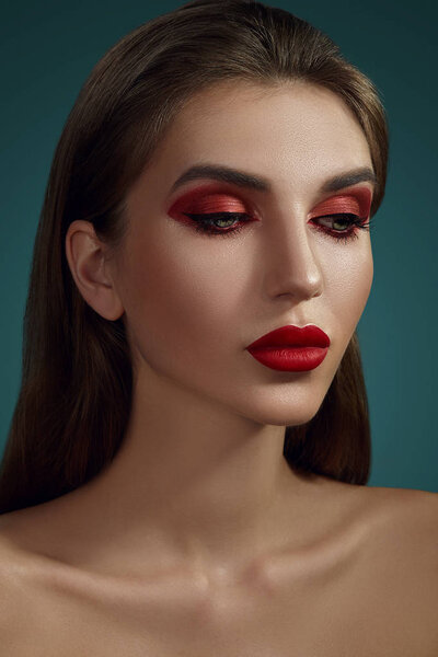 Close-up glamour portrait of a beautiful half-naked model with bright make-up posing over a gray background.