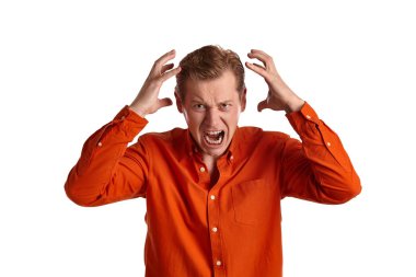 Beyaz stüdyo arka planında izole bir şekilde poz verirken öfkeden kudurmuş gibi davranan turuncu tişörtlü, görkemli genç bir adamın yakın plan portresi. İnsan yüz ifadeleri. Samimi duygular konsepti. Boşluğu kopyala.