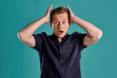 Mavi stüdyo arka planında poz veren havalı bir donanma tişörtü giymiş genç ve çekici bir adamın yakın plan portresi. İnsan yüz ifadeleri. Samimi duygular konsepti. Boşluğu kopyala.