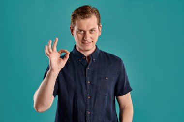 Şık bir donanma tişörtü giymiş, gülümseyen, işaret eden ve mavi stüdyo arka planında poz verirken kameraya bakan genç ve görkemli zencefil pesonun yakın plan portresi. İnsan yüz ifadeleri. Samimi duygular konsepti. Boşluğu kopyala.