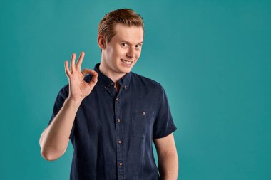 Şık bir donanma tişörtü giymiş genç, atletik bir zencefilin yakın plan portresi. Gülümsüyor, işaret ediyor ve mavi stüdyo arka planında poz verirken kameraya bakıyor. İnsan yüz ifadeleri. Samimi duygular konsepti. Boşluğu kopyala.