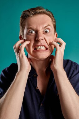 Mavi stüdyo arka planında poz verirken şık bir donanma tişörtü giymiş genç, hoş, kızıl bir erkeğin yakın plan portresi. İnsan yüz ifadeleri. Samimi duygular konsepti. Boşluğu kopyala.