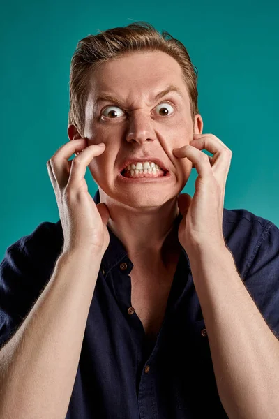 Mavi stüdyo arka planında poz verirken şık bir donanma tişörtü giymiş genç, hoş, kızıl bir erkeğin yakın plan portresi. İnsan yüz ifadeleri. Samimi duygular konsepti. Boşluğu kopyala.