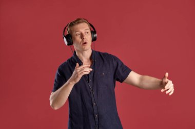 Şık bir donanma tişörtü giymiş, kulaklıkla müzik dinleyen, pembe stüdyo arka planında poz verirken şarkı söyleyen ve dans eden genç ve yakışıklı bir adamın yakın plan portresi. İnsan yüz ifadeleri. Samimi duygular konsepti. Boşluğu kopyala.