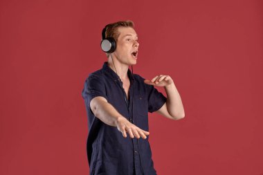 Şık bir donanma tişörtü giymiş genç, yakışıklı bir adamın yakın plan portresi kulaklıkla müzik dinliyor, pembe stüdyo arka planında yan yana poz verirken şarkı söylüyor ve dans ediyor. İnsan yüz ifadeleri. Samimi duygular konsepti. s Kopyala