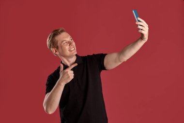 Pembe stüdyo arka planında poz verirken şık siyah tişörtlü, selfie çeken ve gülümseyen genç, zeki bir zencefilin yakın plan portresi. İnsan yüz ifadeleri. Samimi duygular konsepti. Boşluğu kopyala.