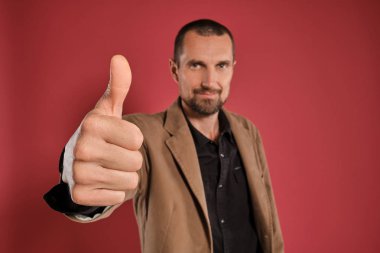 Sakallı ve bıyıklı orta yaşlı bir adam, kırmızı bir arka plan aleyhine poz siyah gömlek ve kahverengi ceket giyer. Samimi duygular kavramı.