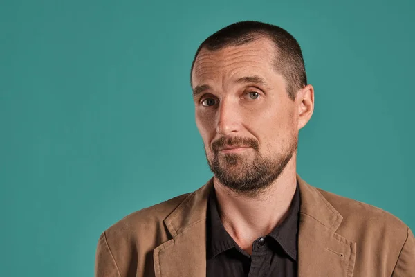 Homme d'âge moyen avec barbe et moustache, porte une chemise noire et une veste brune posant sur un fond bleu. Concept d'émotions sincères . — Photo