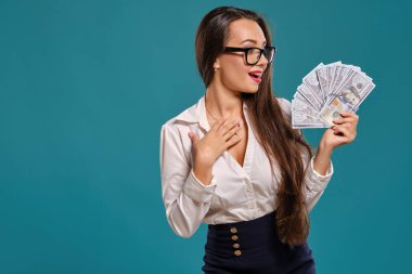Gözlüklü esmer kız, siyah kısa etek ve beyaz bluz giyen mavi bir arka plan karşı yüz dolarlık banknotlar bir fan tutarak poz.