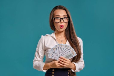 Gözlüklü esmer kız, siyah kısa etek ve beyaz bluz giyen mavi bir arka plan karşı yüz dolarlık banknotlar bir fan tutarak poz.