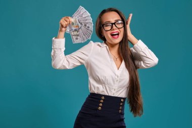 Gözlüklü esmer kız, siyah kısa etek ve beyaz bluz giyen mavi bir arka plan karşı yüz dolarlık banknotlar bir fan tutarak poz.
