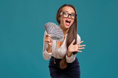 Gözlüklü esmer kız, siyah kısa etek ve beyaz bluz giyen mavi bir arka plan karşı yüz dolarlık banknotlar bir fan tutarak poz.
