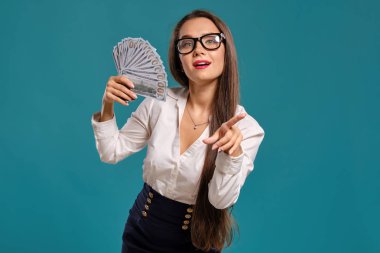 Gözlüklü esmer kız, siyah kısa etek ve beyaz bluz giyen mavi bir arka plan karşı yüz dolarlık banknotlar bir fan tutarak poz.