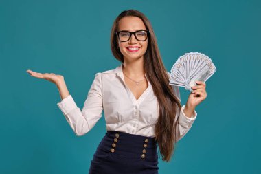 Gözlüklü esmer kız, siyah kısa etek ve beyaz bluz giyen mavi bir arka plan karşı yüz dolarlık banknotlar bir fan tutarak poz.