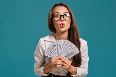 Gözlüklü esmer kız, siyah kısa etek ve beyaz bluz giyen mavi bir arka plan karşı yüz dolarlık banknotlar bir fan tutarak poz.