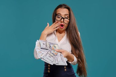 Gözlüklü esmer kız, siyah kısa etek ve beyaz bluz giyen mavi bir arka plan karşı yüz dolarlık banknotlar bir fan tutarak poz.