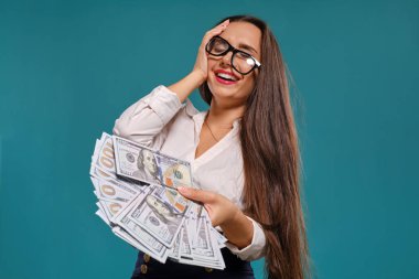 Gözlüklü esmer kız, siyah kısa etek ve beyaz bluz giyen mavi bir arka plan karşı yüz dolarlık banknotlar bir fan tutarak poz.