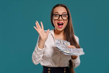 Gözlüklü esmer kız, siyah kısa etek ve beyaz bluz giyen mavi bir arka plan karşı yüz dolarlık banknotlar bir fan tutarak poz.