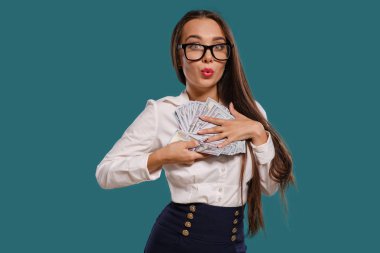 Gözlüklü esmer kız, siyah kısa etek ve beyaz bluz giyen mavi bir arka plan karşı yüz dolarlık banknotlar bir fan tutarak poz.