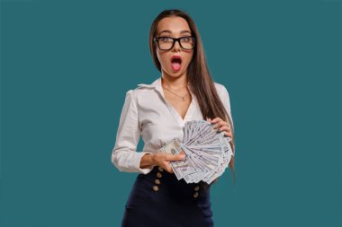Gözlüklü esmer kız, siyah kısa etek ve beyaz bluz giyen mavi bir arka plan karşı yüz dolarlık banknotlar bir fan tutarak poz.