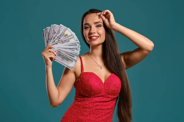 Brunetka dziewczyna z długimi włosami, ubrana w seksowną czerwoną sukienkę pozuje gospodarstwa fan stu rachunków dolara na niebieskim tle. — Zdjęcie stockowe