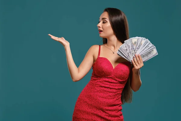 Brunetka dziewczyna z długimi włosami, ubrana w seksowną czerwoną sukienkę pozuje gospodarstwa fan stu rachunków dolara na niebieskim tle. — Zdjęcie stockowe