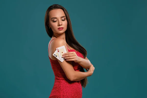 Ragazza bruna con i capelli lunghi, indossa un abito rosso sexy è in posa tenendo due carte da gioco in mano, sfondo blu . — Foto Stock
