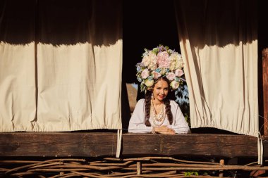 Beyaz ukrayna otantik ulusal kostüm ve çiçek çelenk esmer kız pencereden dışarı bakıyor.