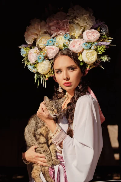 Bruna ragazza in un bianco ucraino autentico costume nazionale e una corona di fiori è in posa per la fotocamera. Primo piano . — Foto Stock